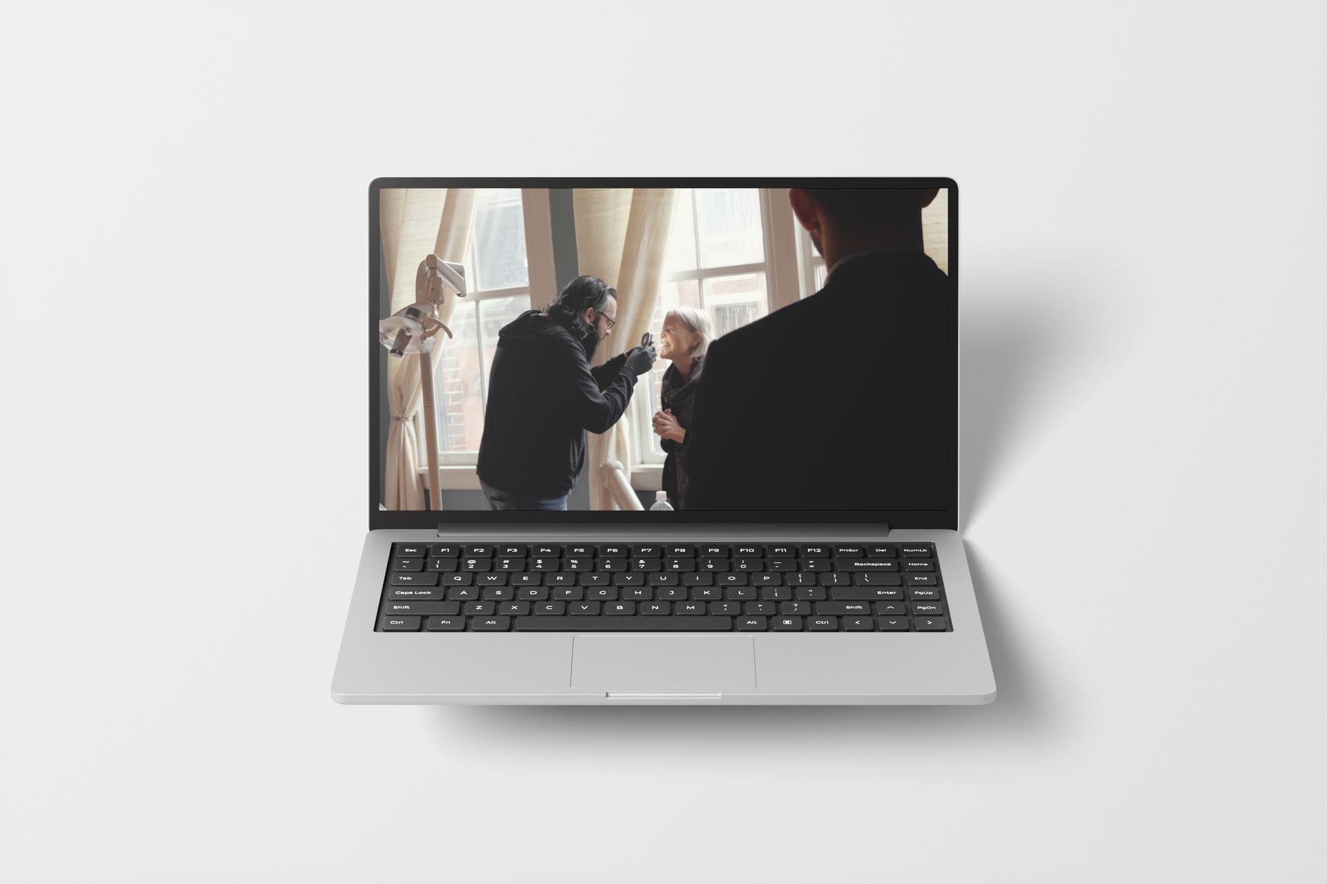 Laptop displaying a video of two people, one holding a camera, in front of a window.