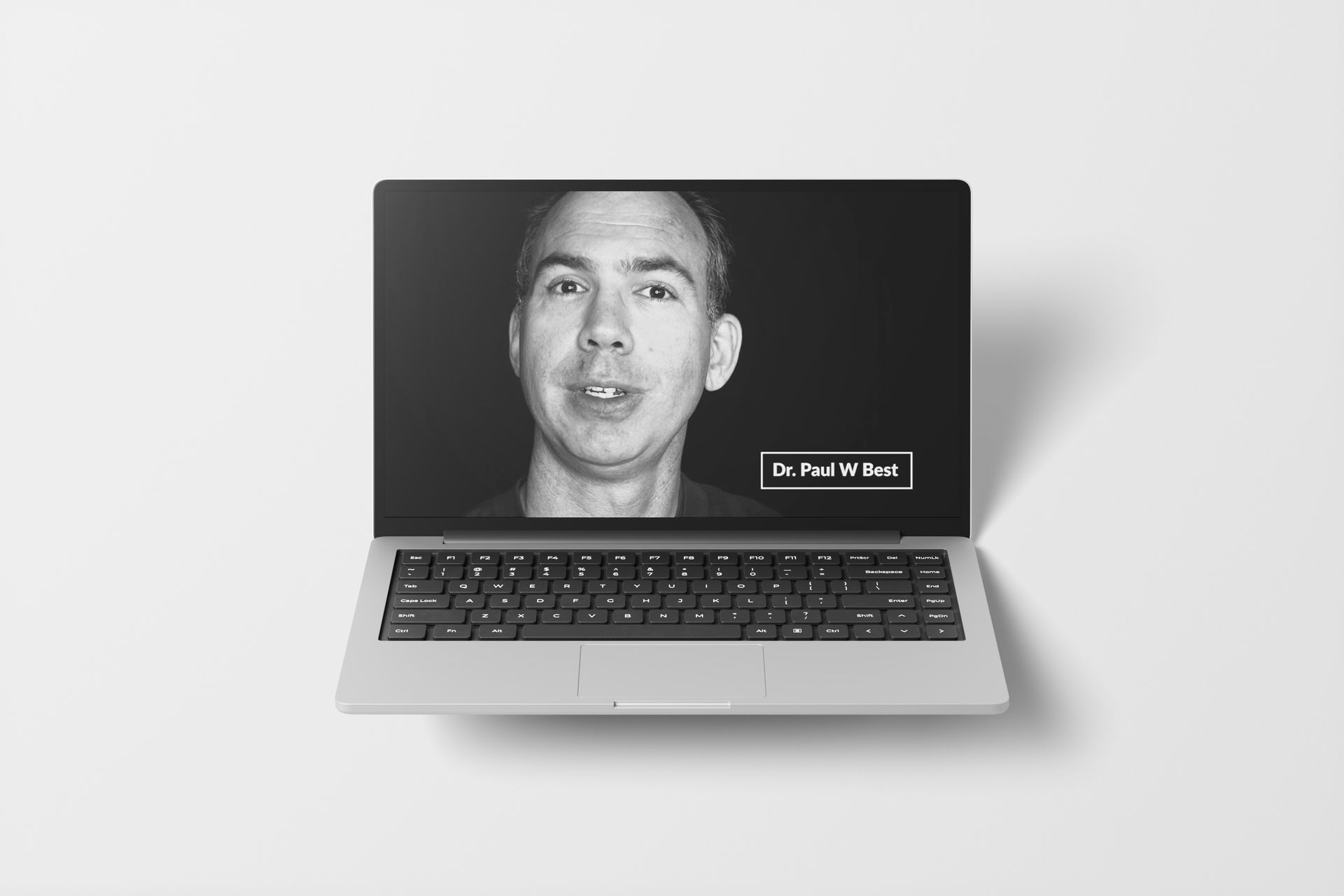 Laptop displaying a grayscale video of a man speaking, with a text box that reads 