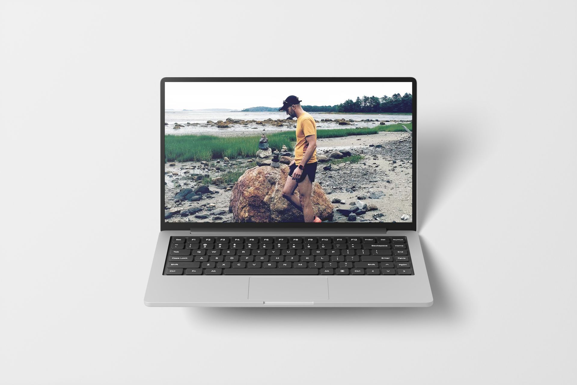 Laptop displaying a person walking on a rocky shoreline near the water.