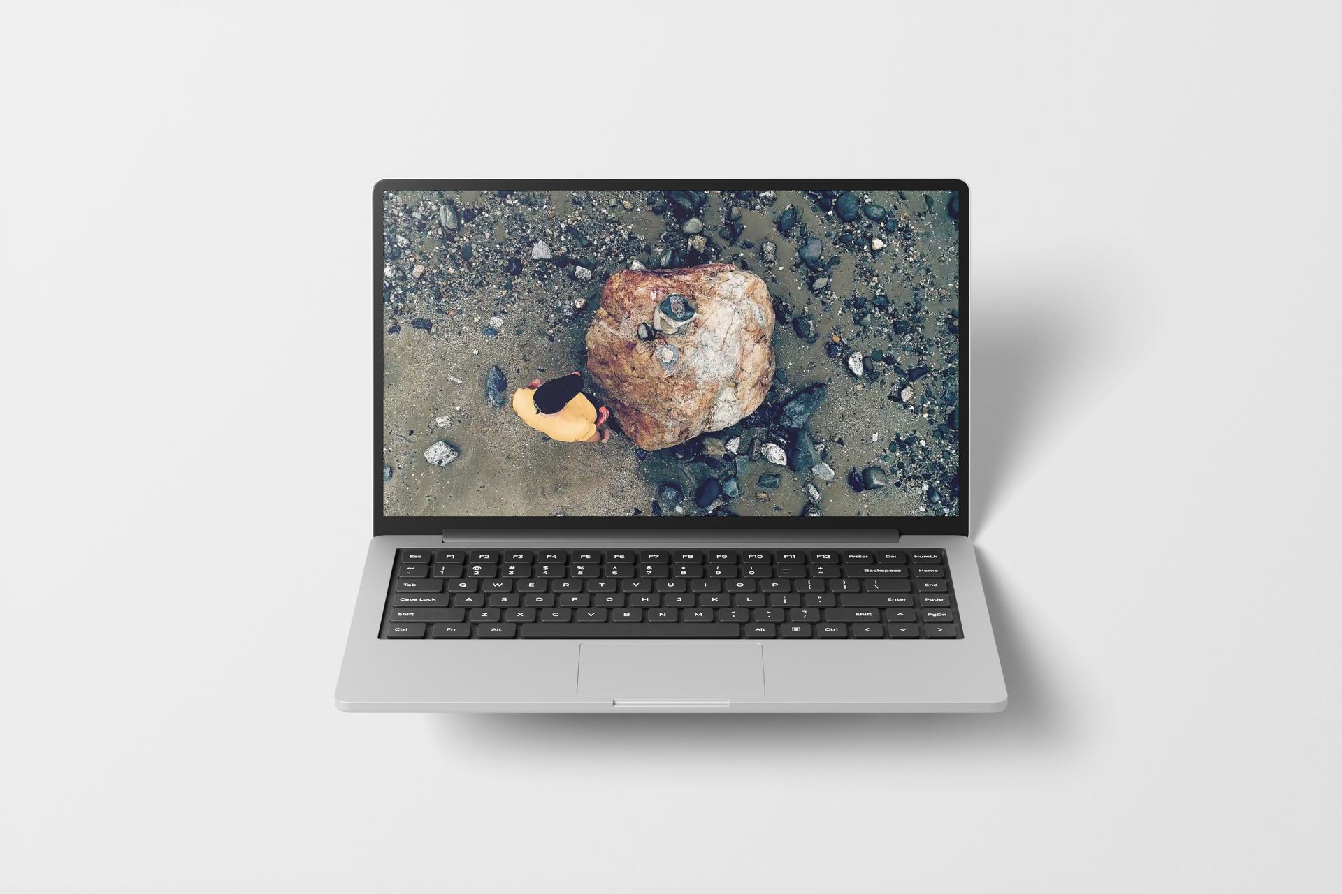 Laptop displaying a close-up image of a rock on a sandy surface, top view on a white background.