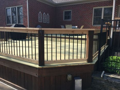 a wooden deck with a metal railing in front of a brick house
