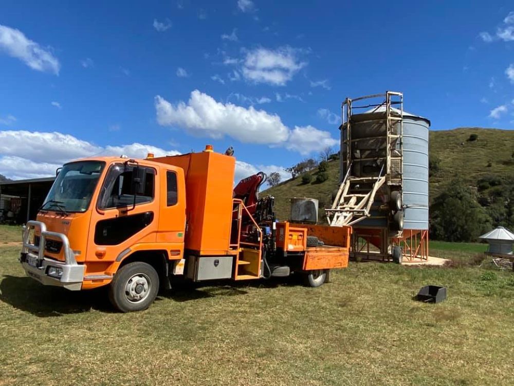 An Orange Truck is Parked in a Grassy Field Next to a Silo — Wallamore Grading & Packaging In Wallamore, NSW