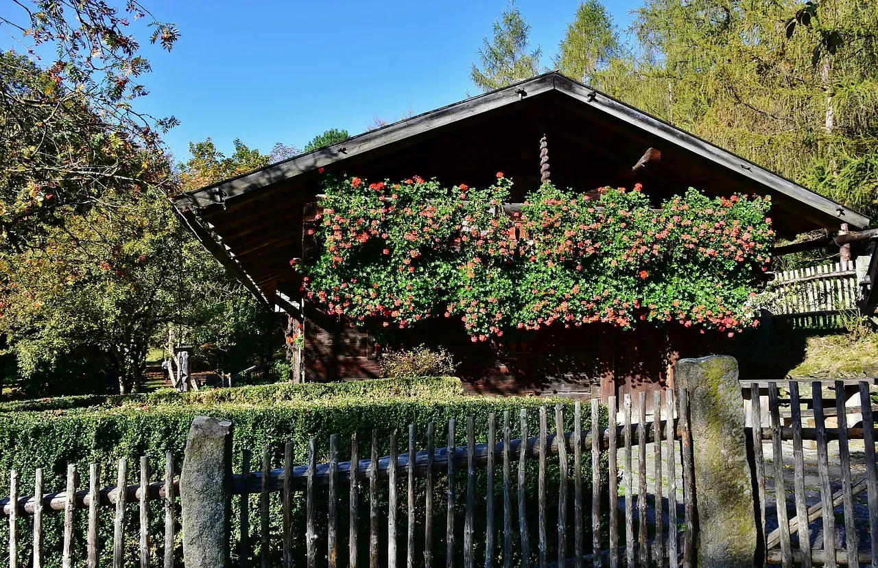 A wooden fence surrounds a house with flowers on the roof
