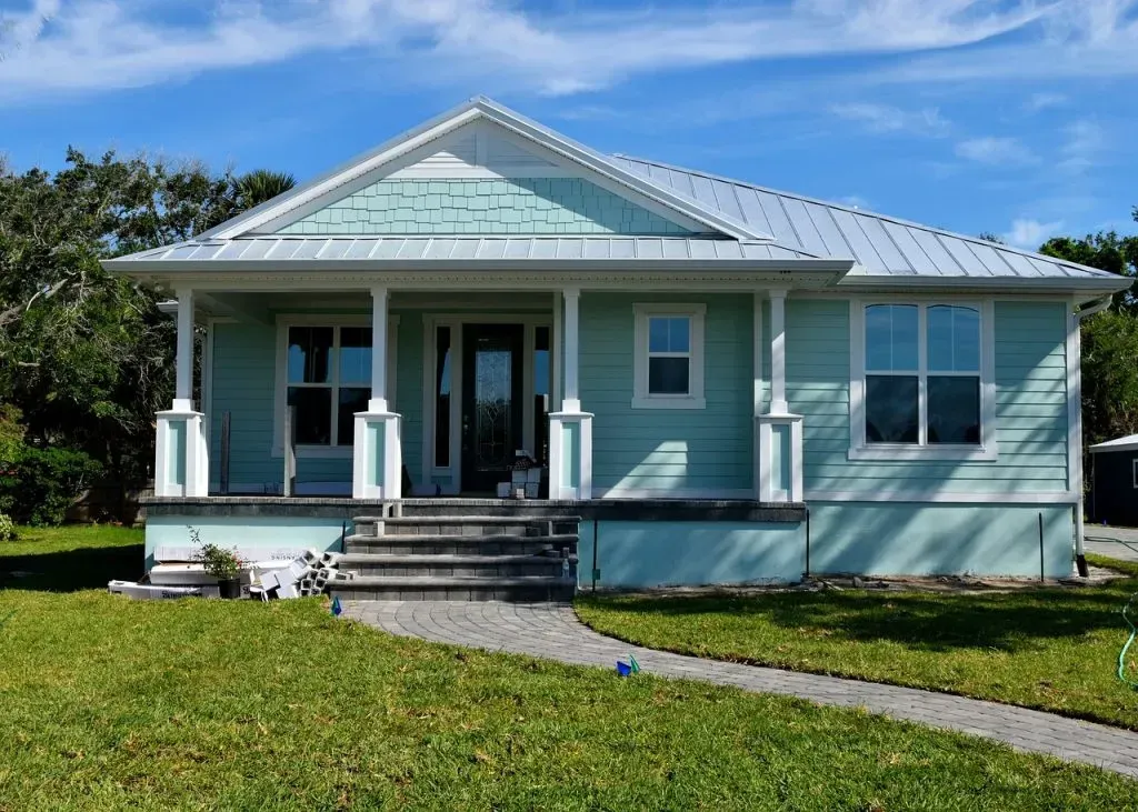 A green house with a white porch and stairs is sitting on top of a lush green lawn.