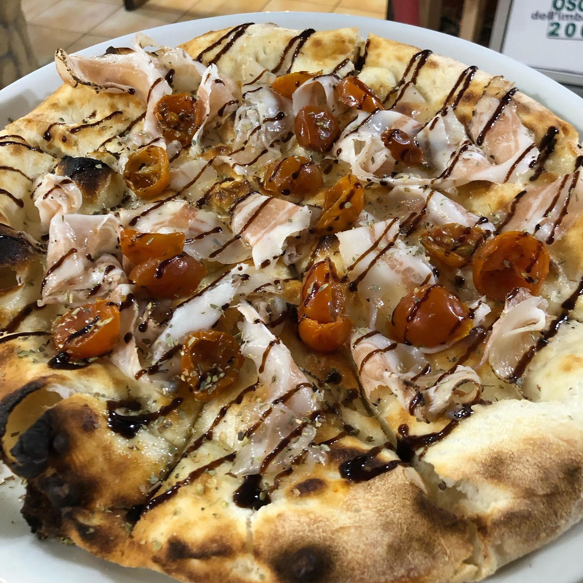 Una pizza cotta nel forno a legna, condita con sottili fette di salumi, pomodorini arrostiti e un filo di glassa balsamica.