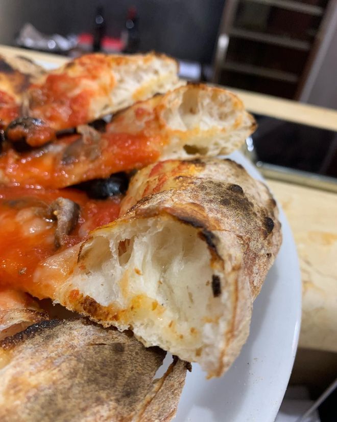 Pizzaiolo al lavoro con impasto fresco e forno a pietra.