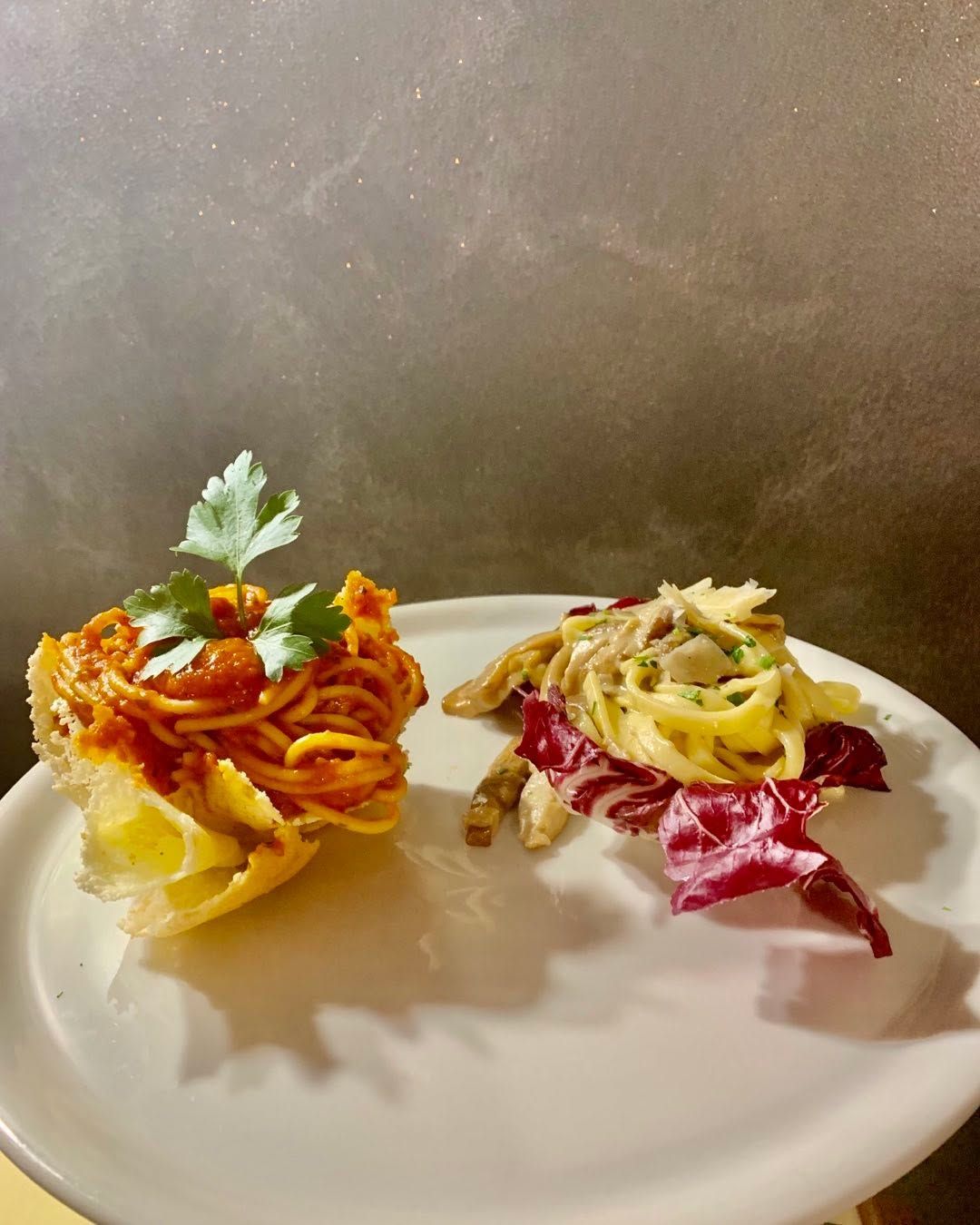 Un piatto bianco contenente due porzioni di pasta: una al sugo di pomodoro guarnita con prezzemolo, l'altra su foglie di radicchio.