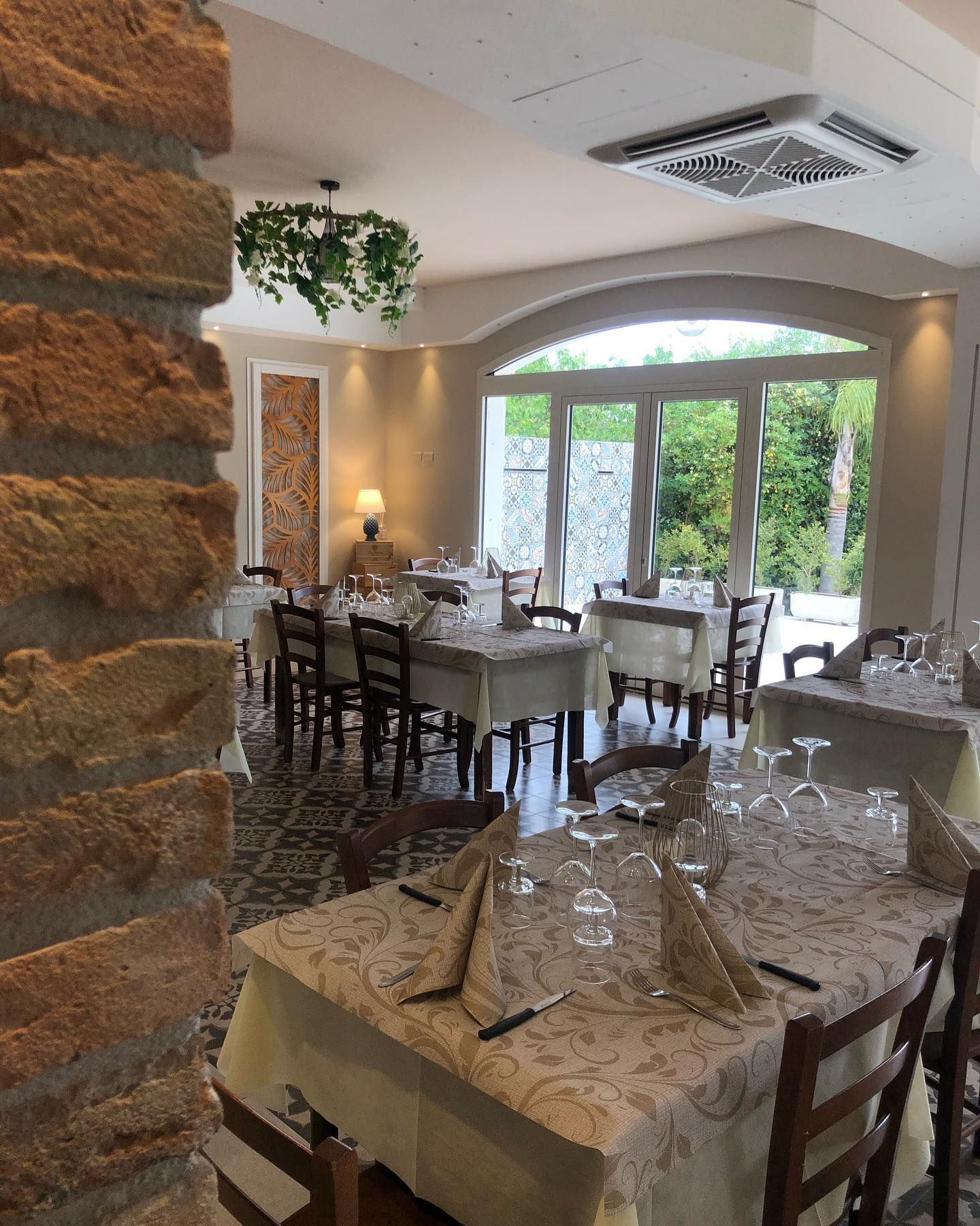 In un ristorante con un pilastro in mattoni, i tavoli da pranzo sono vuoti, ricoperti da tovaglie beige, tovaglioli piegati e bicchieri.