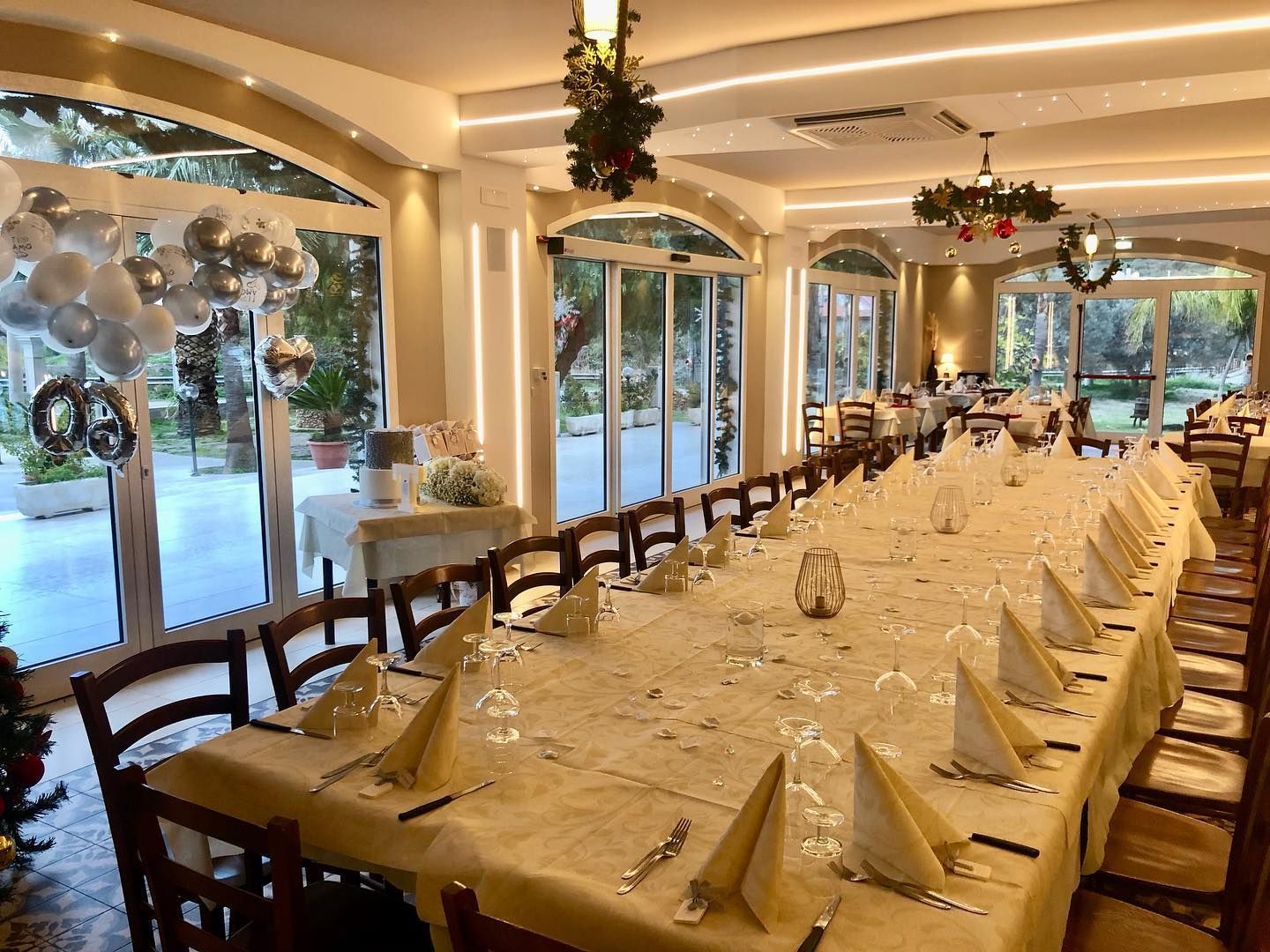 Una sala per banchetti con un lungo tavolo ricoperto di carta color crema, apparecchiato per un evento formale, caratterizzato da decorazioni festive e porte a vetri.