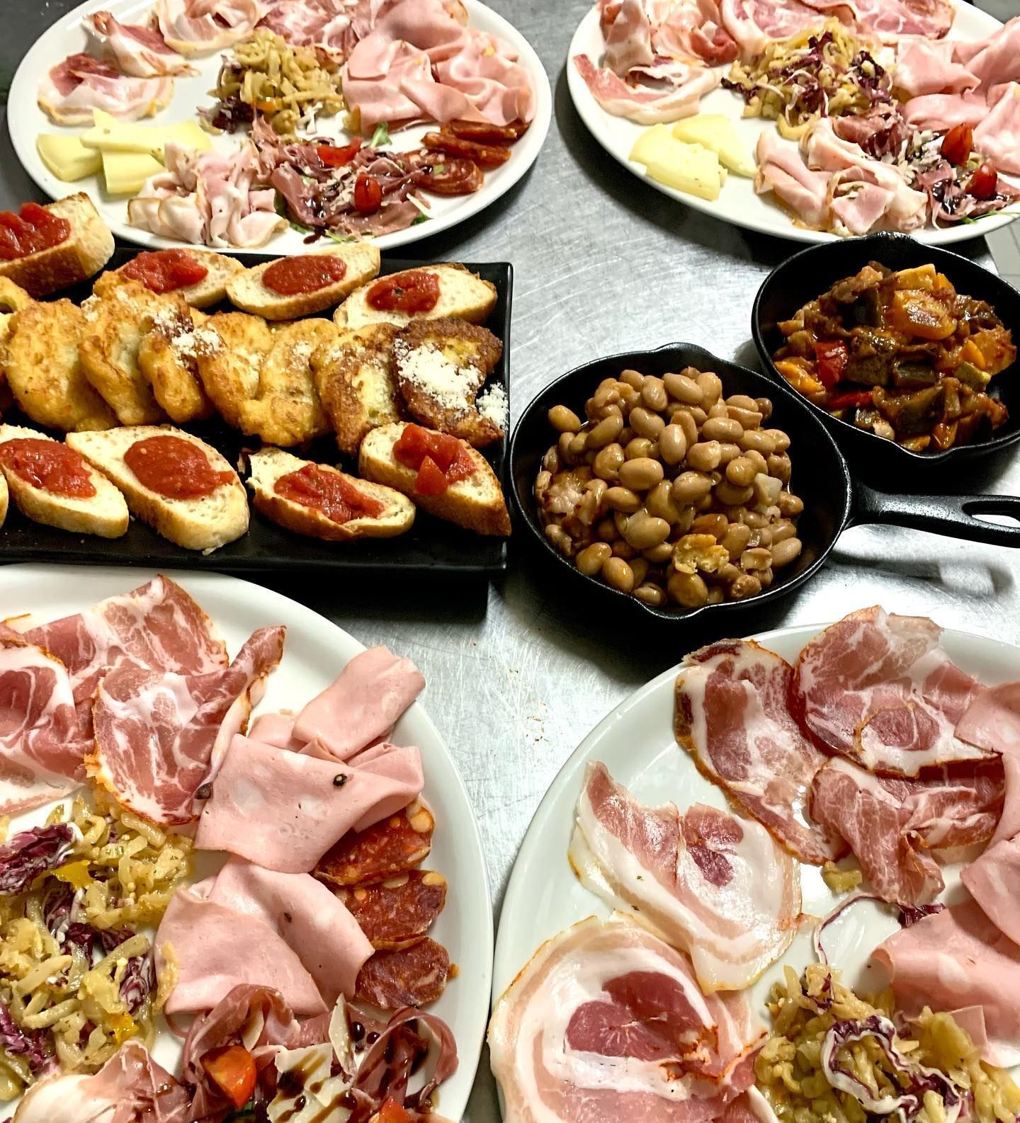 Numerosi piatti con un assortimento di salumi, formaggi, antipasti e piccole padelle in ghisa contenenti fagioli e verdure.