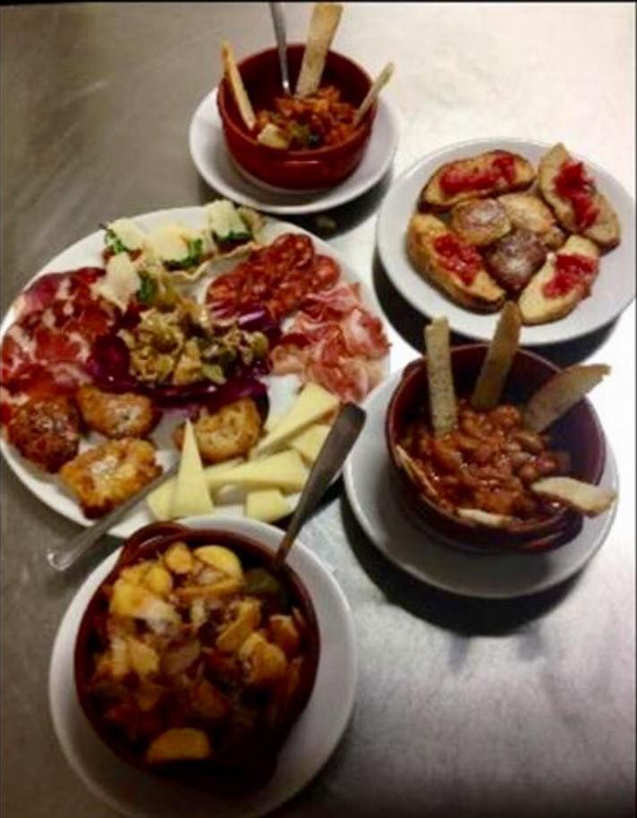 Un assortimento di tapas, tra cui salumi, formaggi, pane e ciotole di fagioli e patate stufate, disposti su un tavolo.