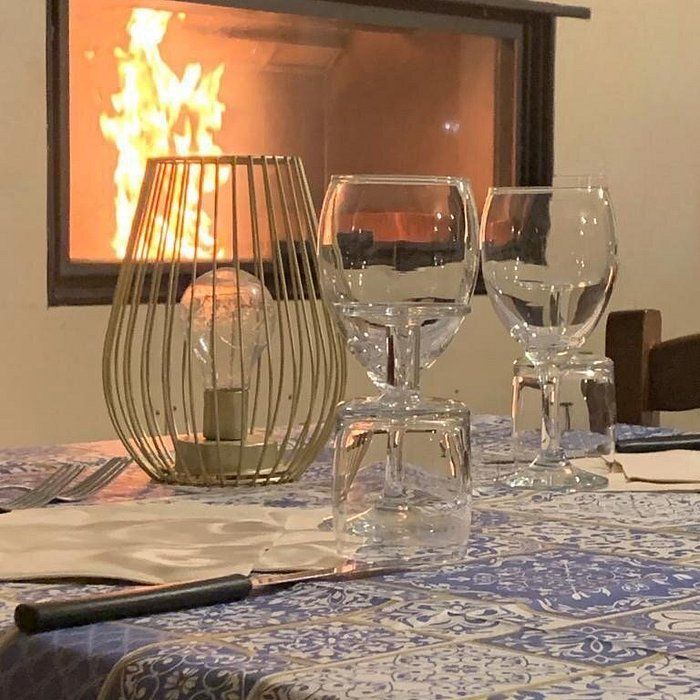 Una tavola accogliente apparecchiata con una lanterna in filo dorato e calici da vino, sullo sfondo di un caldo camino acceso.