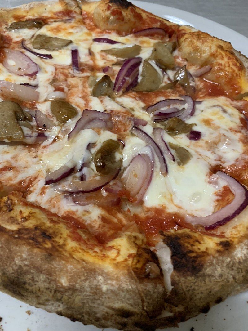 Primo piano di una pizza condita con fette di cipolla rossa, olive verdi e formaggio fuso su una base di salsa di pomodoro.