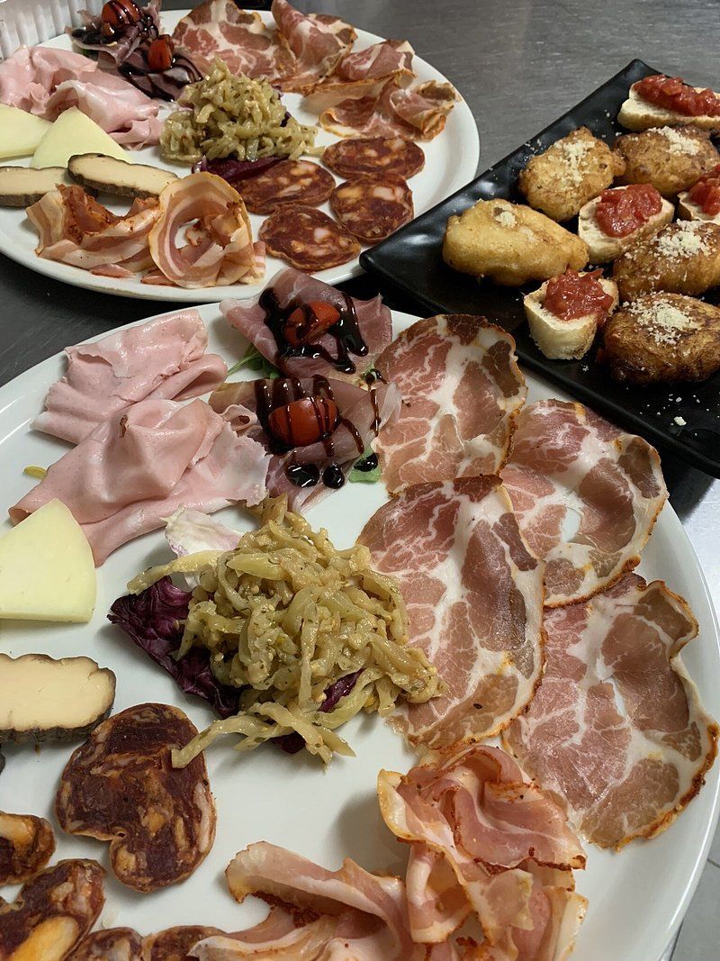 Due grandi vassoi bianchi con salumi, formaggi e contorni di verdure italiane, accanto a un vassoio di pane tostato con vari condimenti.