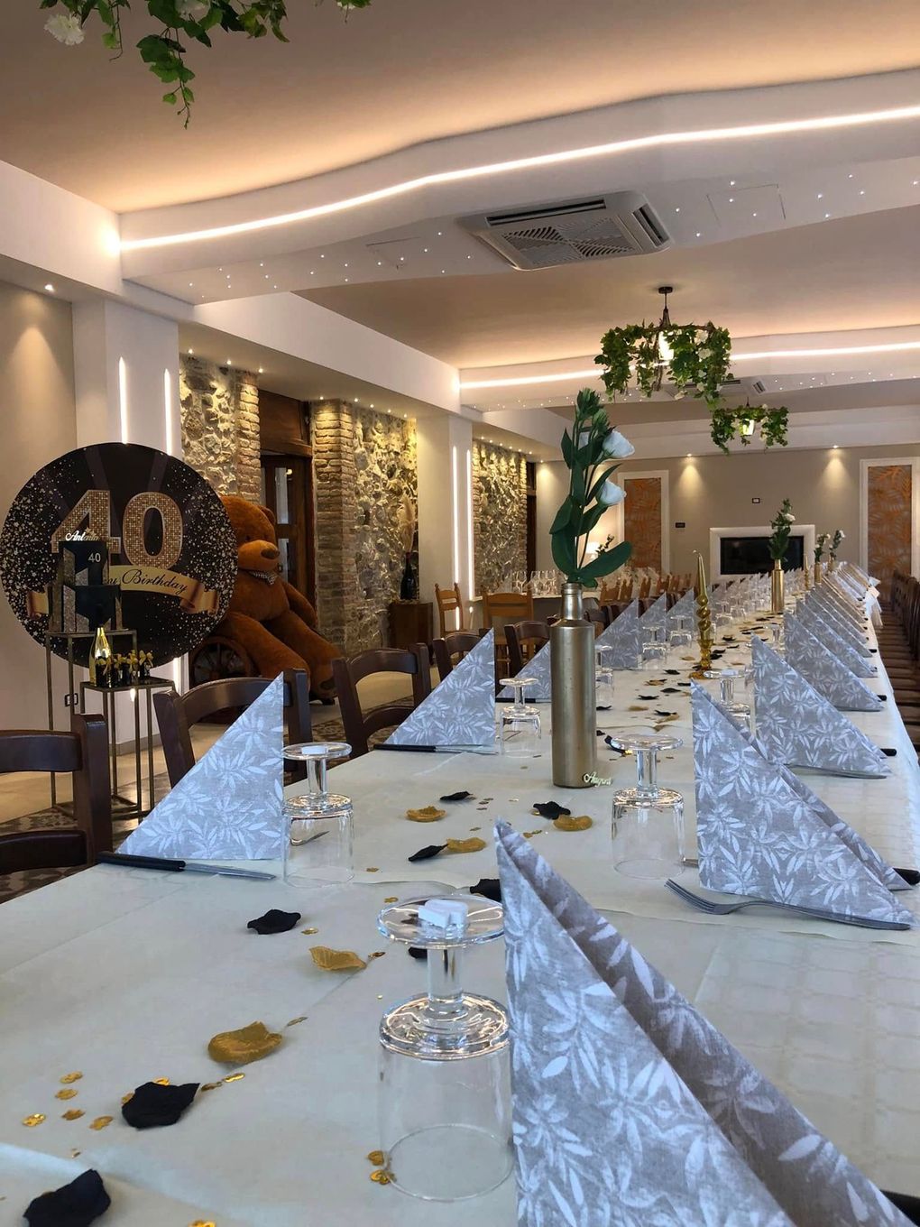 Un lungo tavolo da pranzo apparecchiato per un evento formale, con tovaglioli decorati, dettagli dorati e un cartello con il numero