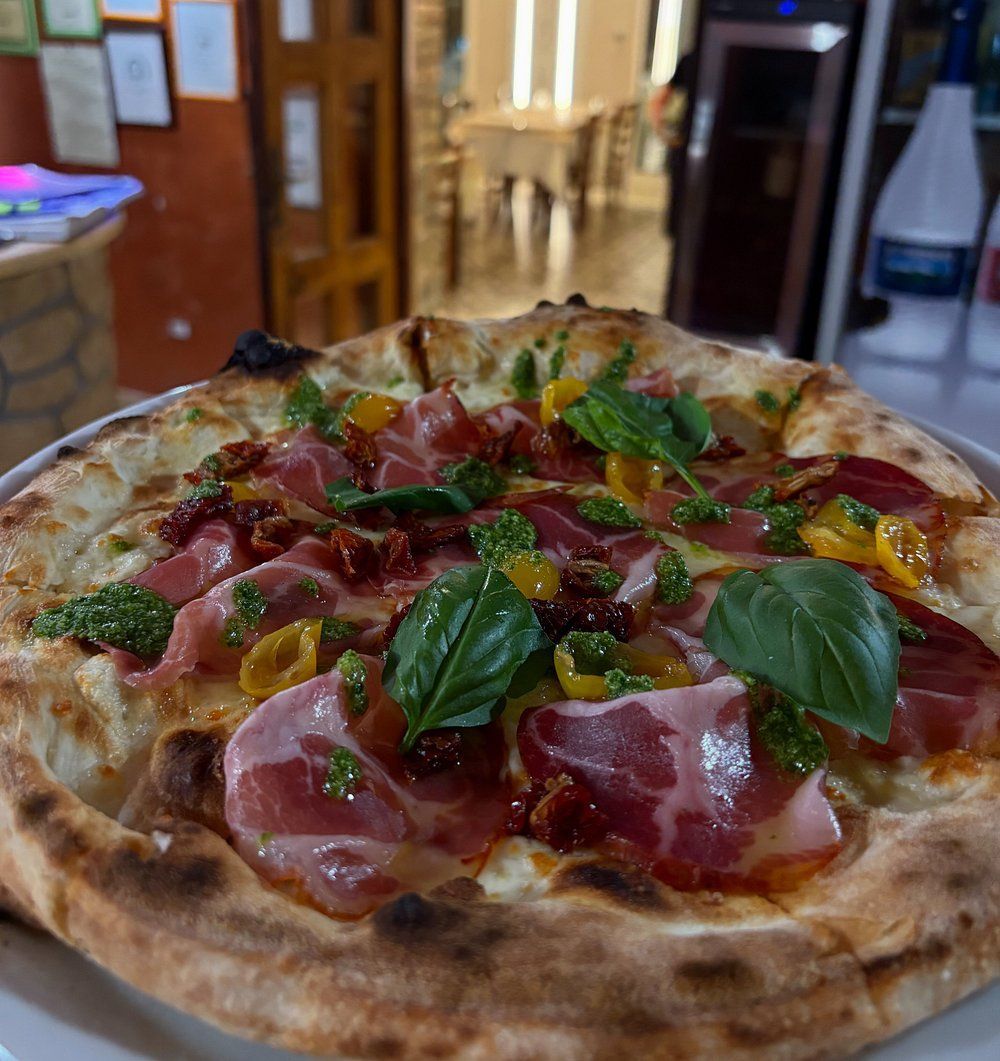 Una pizza condita con salumi, pomodori secchi, pesto e foglie di basilico fresco, servita al tavolo di un ristorante.