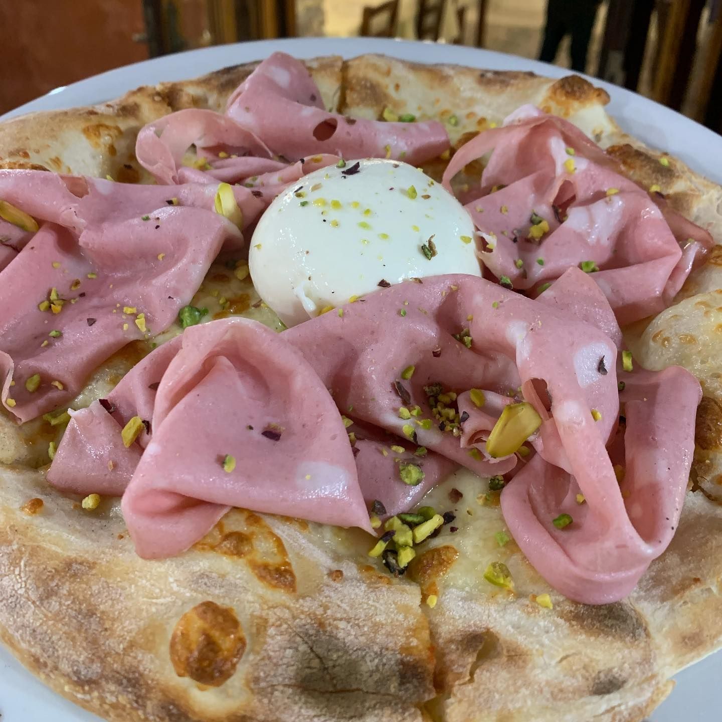 Una pizza condita con mortadella, una palla centrale di burrata e pistacchi tritati sparsi qua e là.