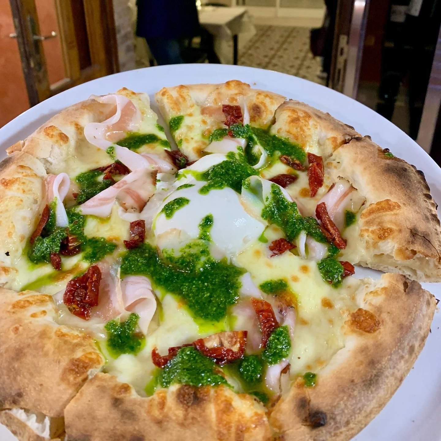 Una pizza gourmet con pomodori secchi, pesto e sottili fette di salumi, il tutto guarnito con una cucchiaiata di formaggio cremoso.