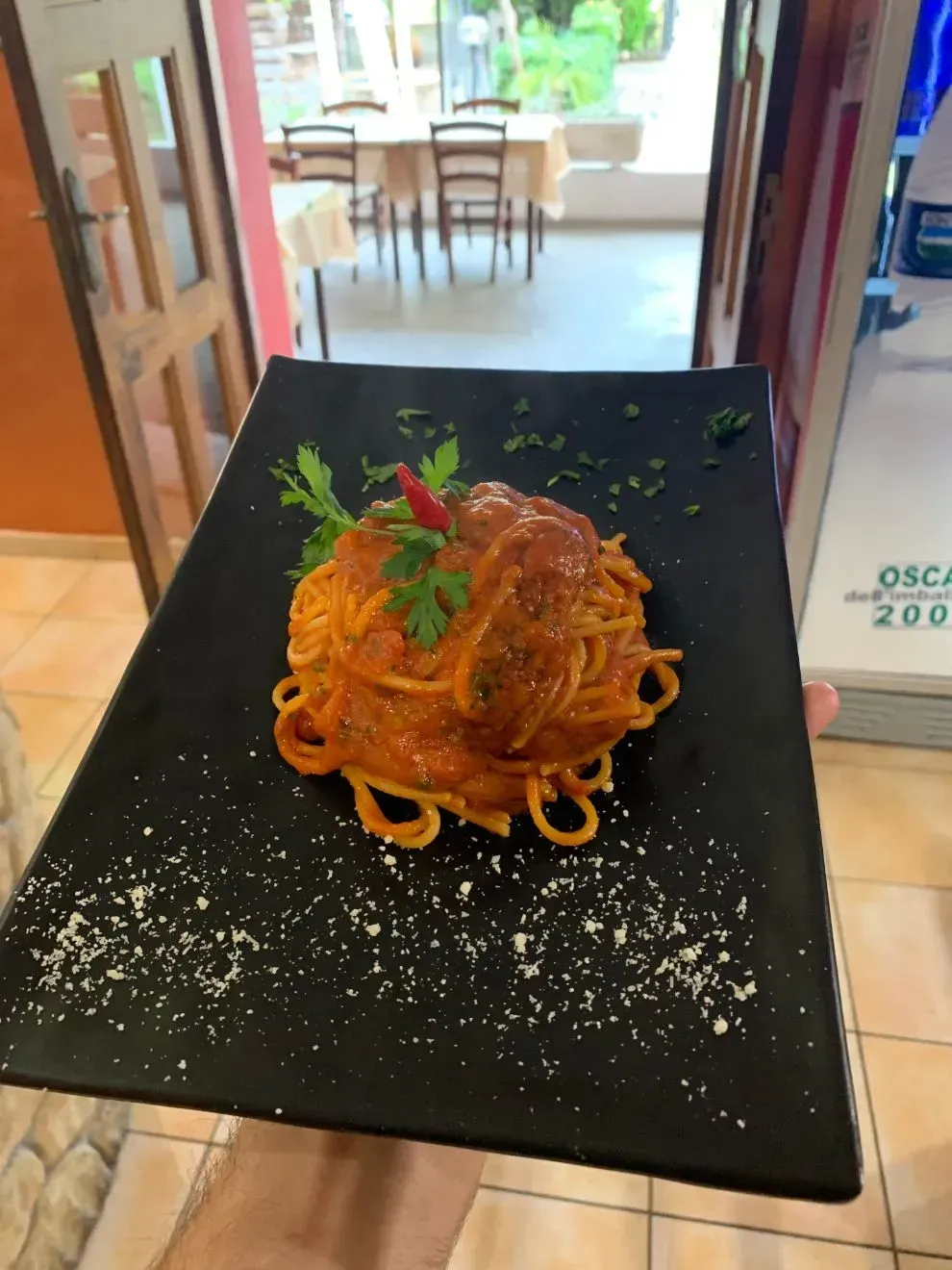 Un piatto di spaghetti al sugo di pomodoro, guarnito con prezzemolo fresco e un peperoncino, sullo sfondo sfocato di un ristorante.