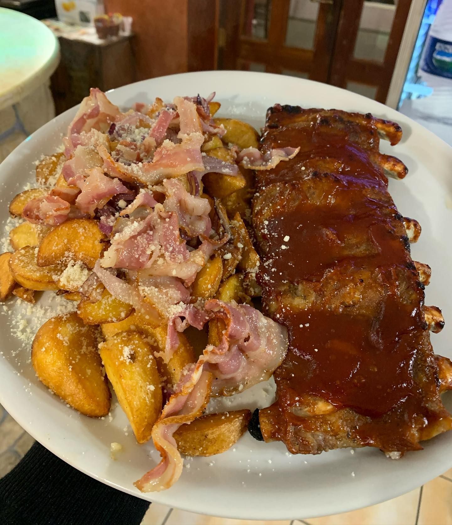 Un piatto bianco con una costata di maiale alla griglia e una generosa porzione di spicchi di patate conditi con pancetta e formaggio.