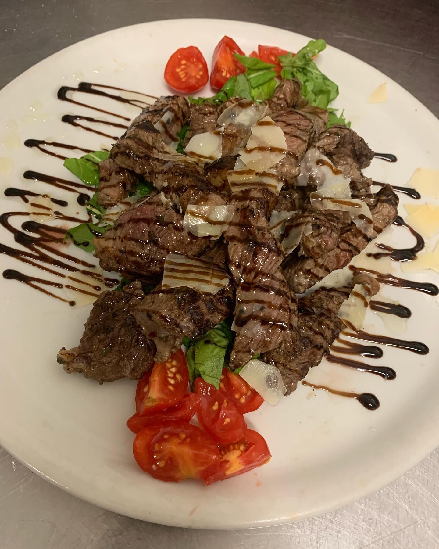 Striscioline di bistecca grigliate servite su un letto di verdure e pomodorini, condite con glassa di aceto balsamico e scaglie di parmigiano.