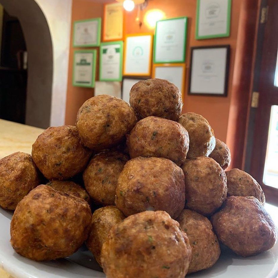 Un grande mucchio di polpette fritte, di un bel colore dorato, è impilato su un piatto bianco davanti a una parete con dei certificati incorniciati.