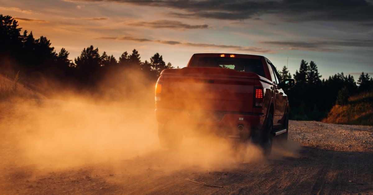 A truck driving along a dirt path. The sun is low and there is an orange tint to the surroundings.