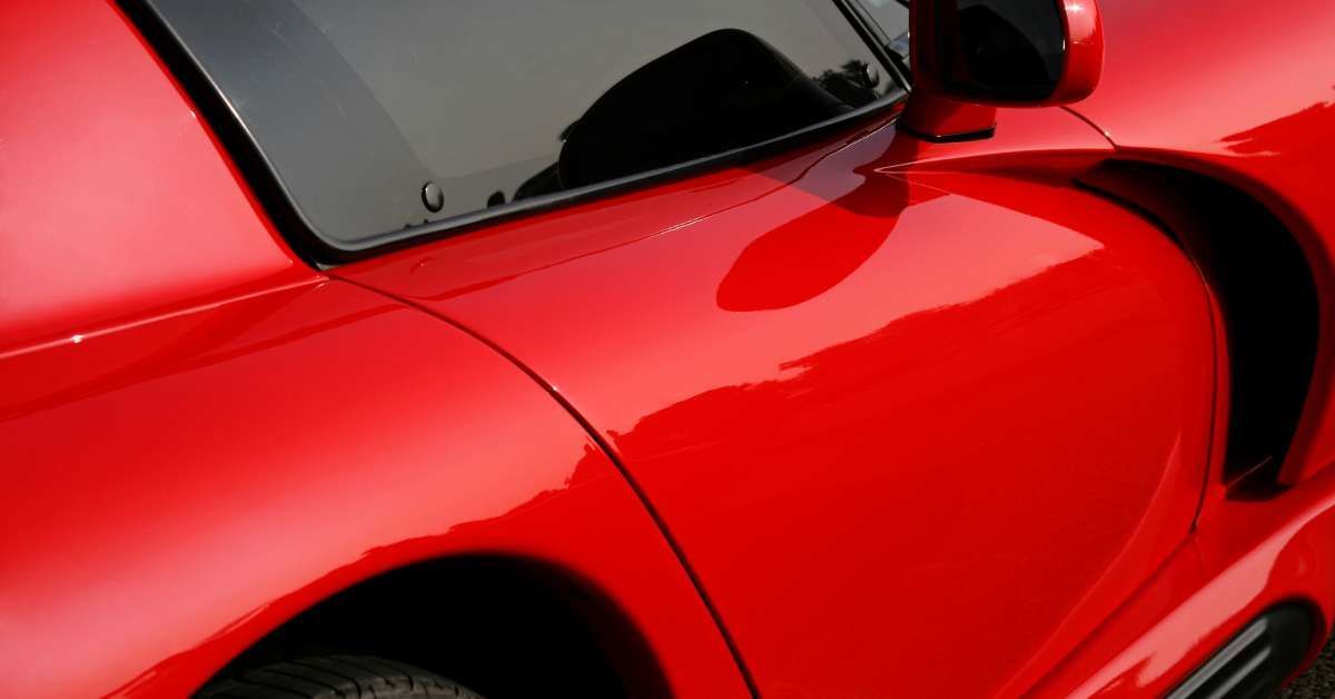 A bright red sports car with slightly tinted windows and a pristine, shiny exterior that reflects its surroundings.