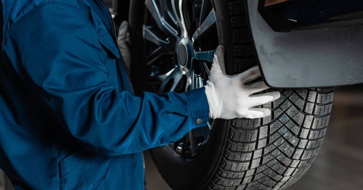 A mechanic wearing a blue suit and white gloves is carefully installing a tire on a vehicle in their shop.