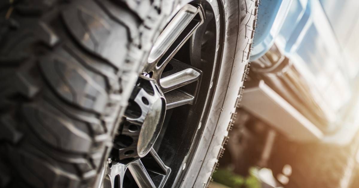 The sun is shining brightly on a blue truck that is parked. The tires have deep treads for off-roadi