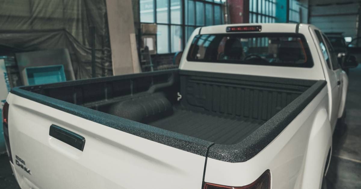 A white truck with a gray truck bed is parked in a large building. Another white truck is in front.