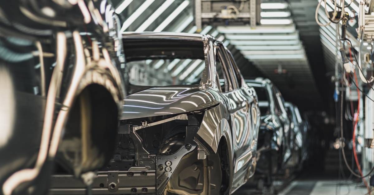 A line of clean car bodies are moving down the production line inside of a large facility with bright lights.