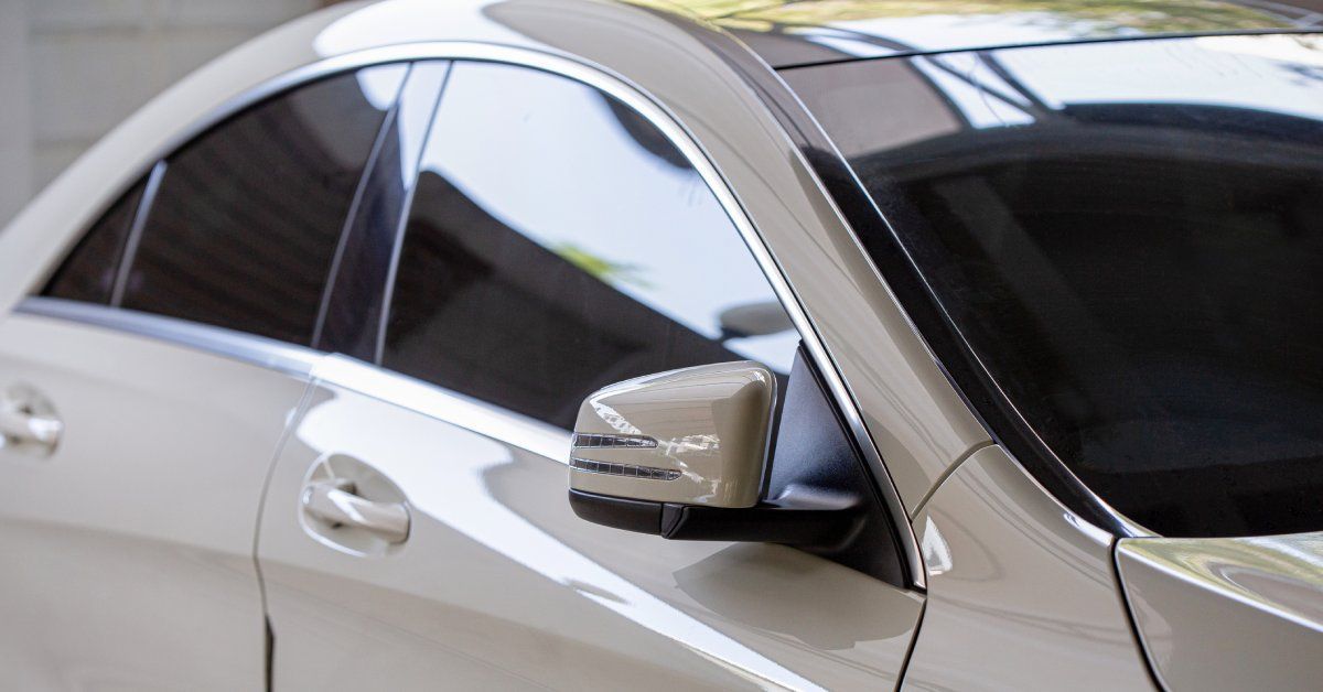 A clean, luxurious white car is parked in a darkly lit area outside. The car windows are fully tinted.