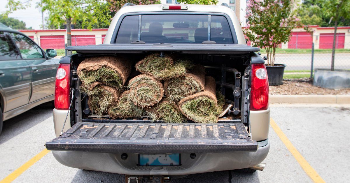 A parked pickup truck with a tonneau cover installed on top of the bed. The truck bed is full of grass.