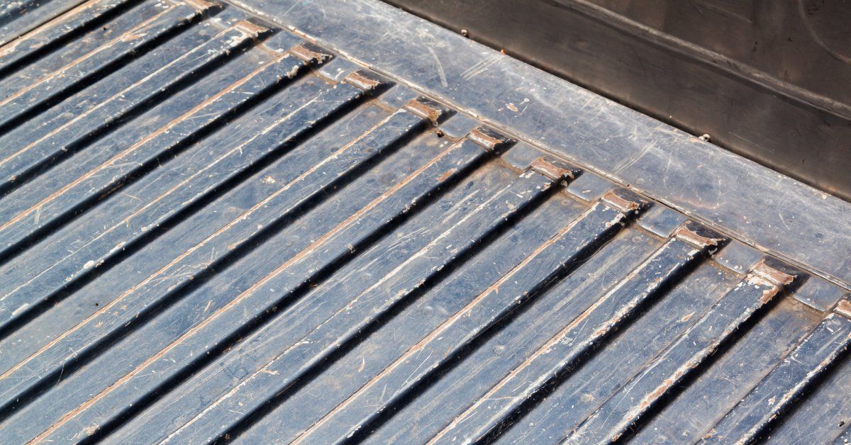 An empty truck bed with a black surface. The surface is almost entirely covered in large dents and scrapes.