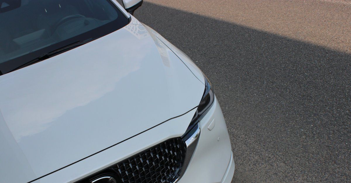 A white car is parked outside on the street. The weather is sunny but the car is parked in the cool shade.