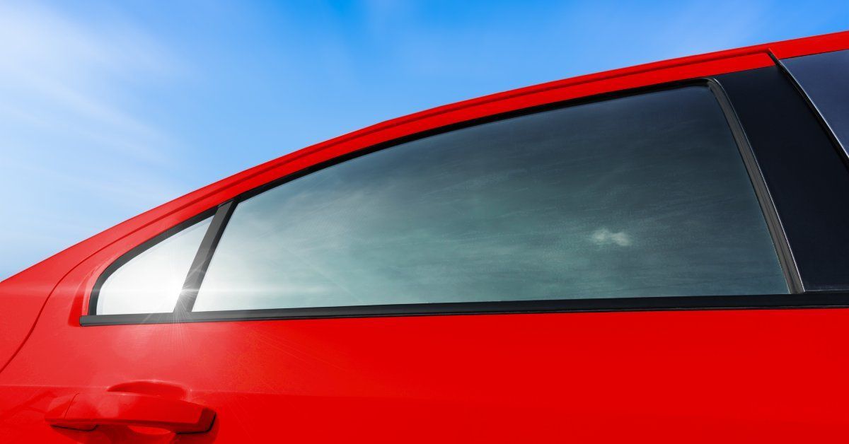 A red car parked outside on a sunny day with blue skies above. The car windows are tinted.