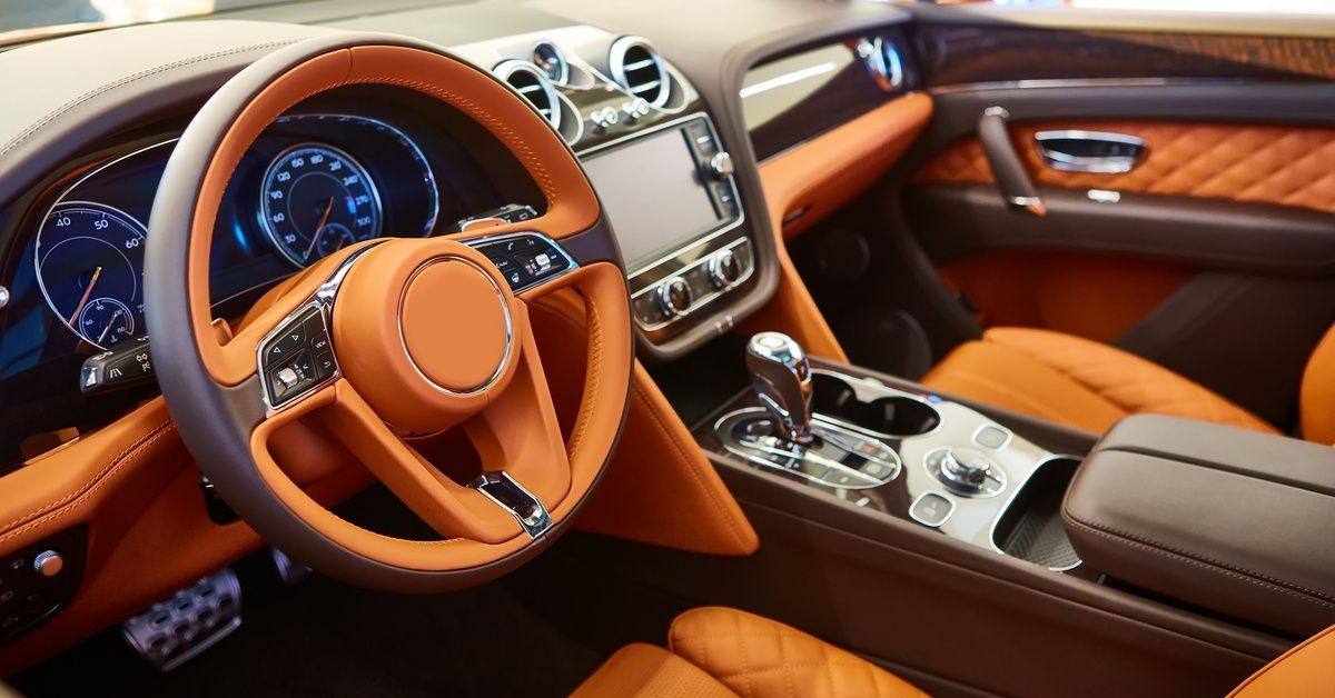 The interior of a luxury car. The car has brown leather seats and a leather steering wheel to match.