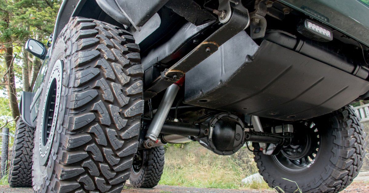 A vehicle with a clean, robust suspension system is parked outside. A white fence is visible in the distance.