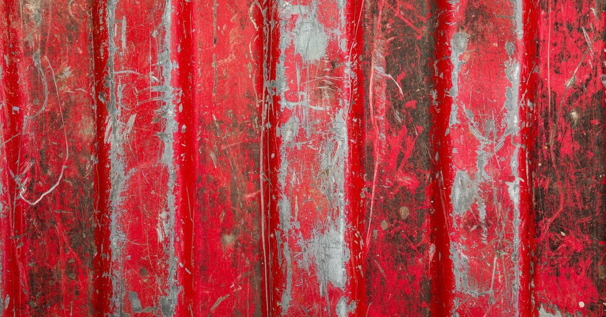 The bumpy bed of a red pickup truck. The red paint in the truck bed is scratched and covered in harsh dents.