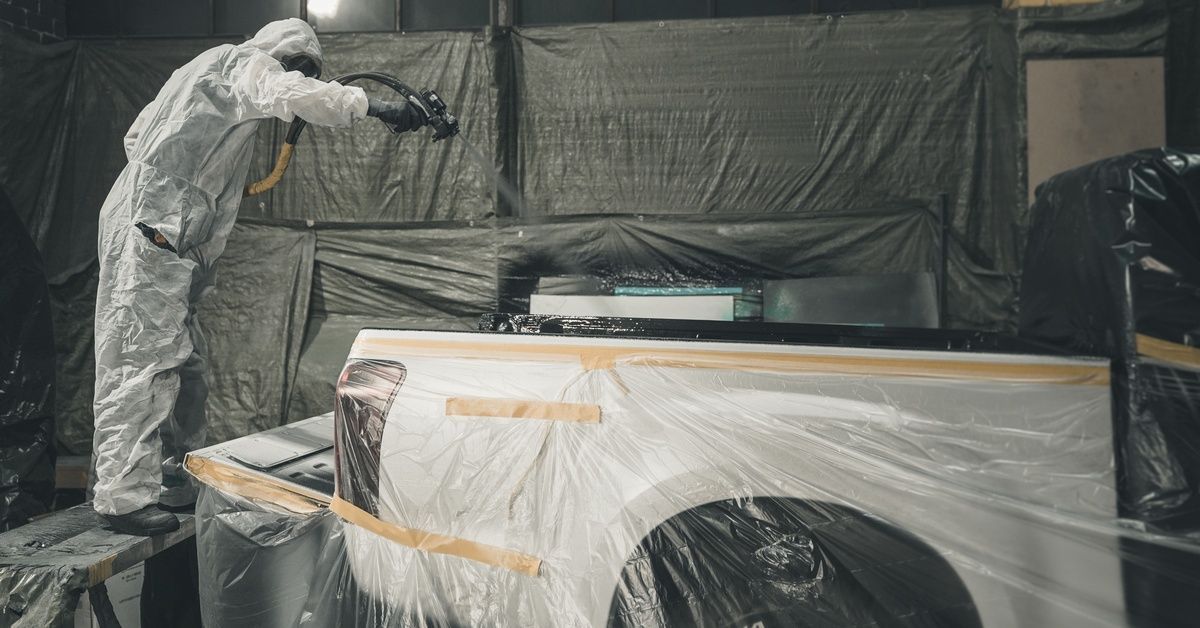 A professional applying a spray-in bedliner to the bed of a white pickup truck.
