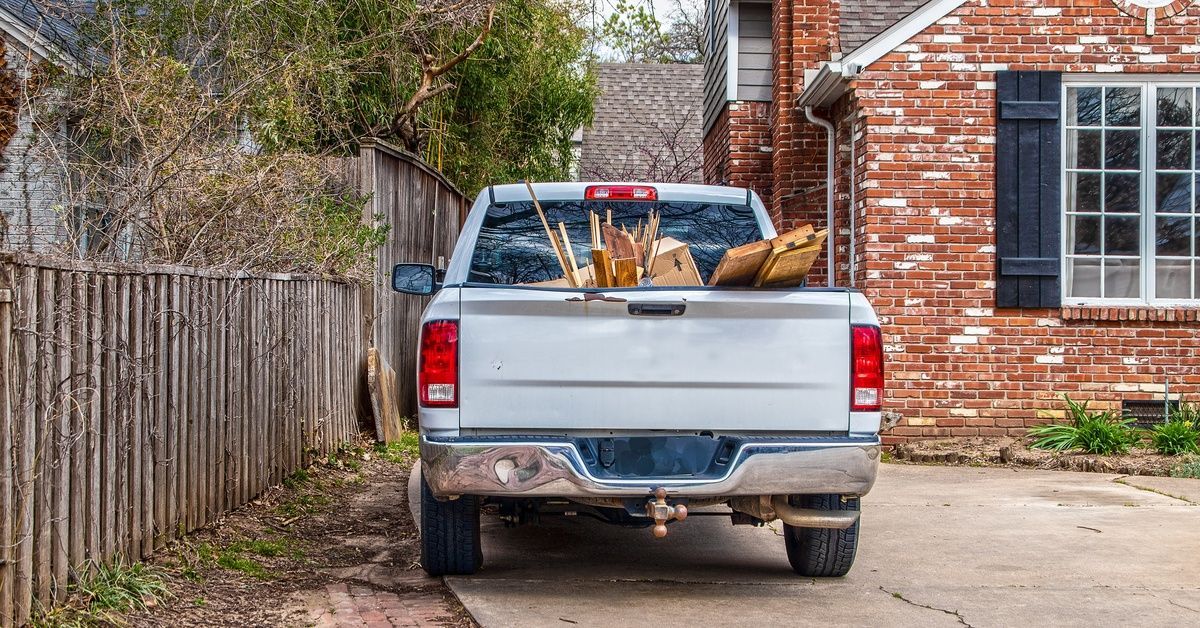 A gray pickup truck parked in a home’s cracked driveway. The bed is full of wooden construction materials.