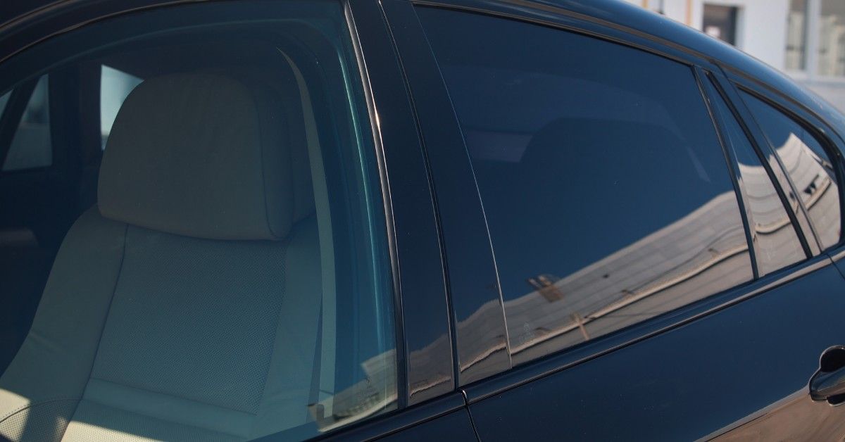 A shiny black car parked outside during the daytime. The car has tinted rear windows that partially block the backseat.