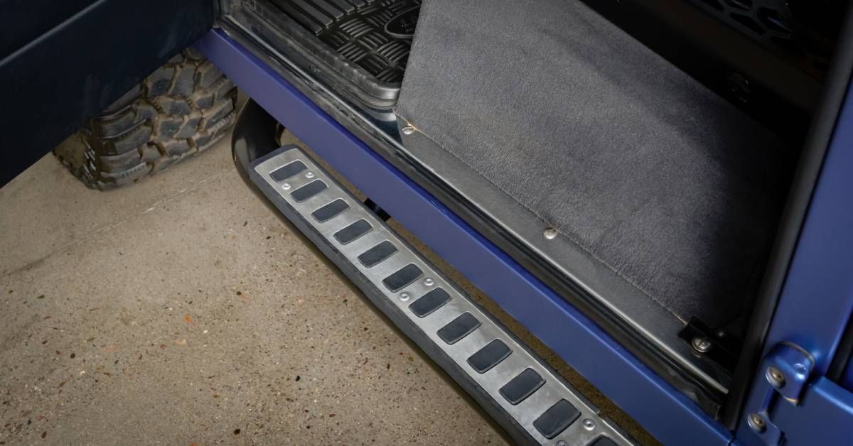 A large blue truck with a running board installed on its side. The truck’s driver-side door is open.