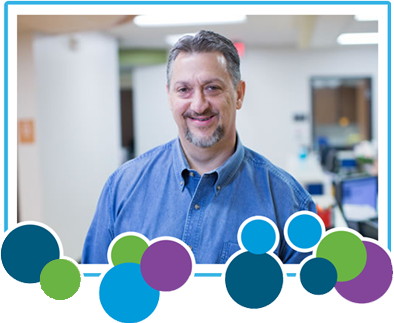 Man smiling in a blue shirt, office setting.