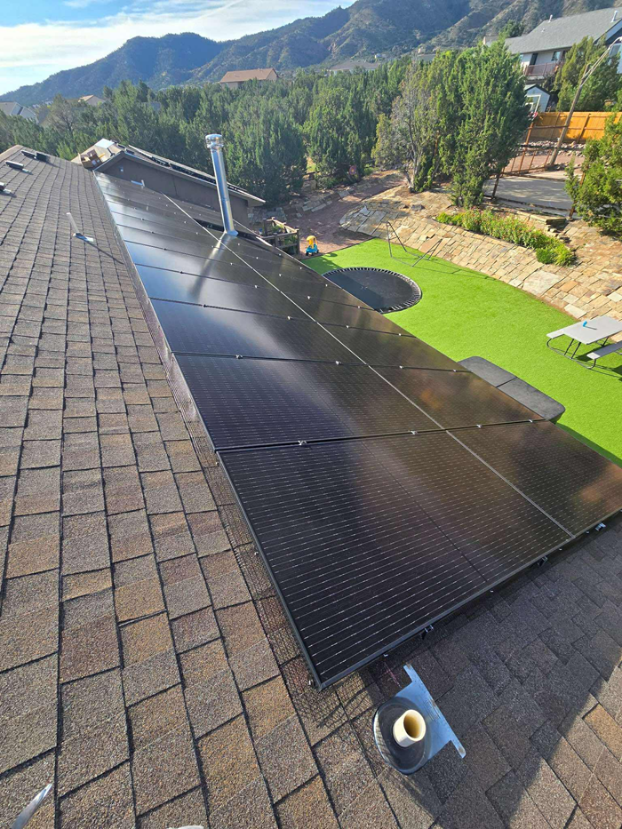 Solar panels installed on a shingled roof, with mountain views in the background.