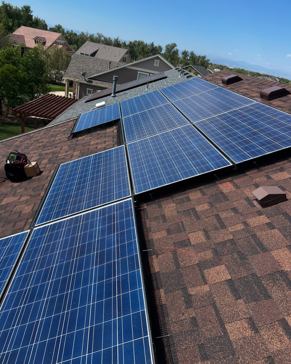 Solar panels installed on a brown shingle roof under a blue sky.