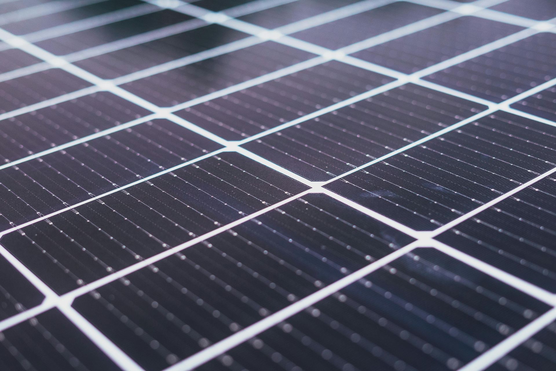 Close-up of a solar panel with dark squares and white grid lines, capturing sunlight.