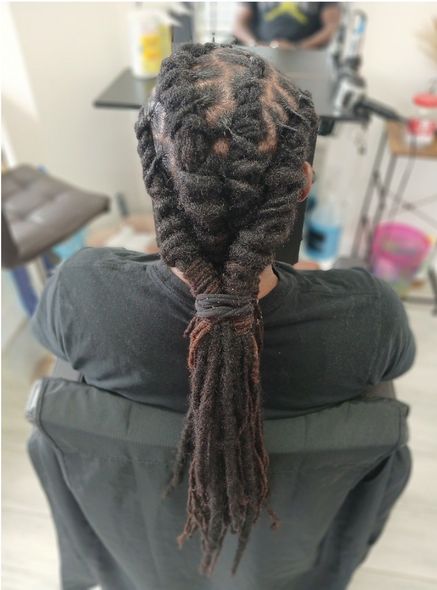 Person in a black shirt with dreadlocks twisted into an updo, ponytail. Indoors, seated in a chair.