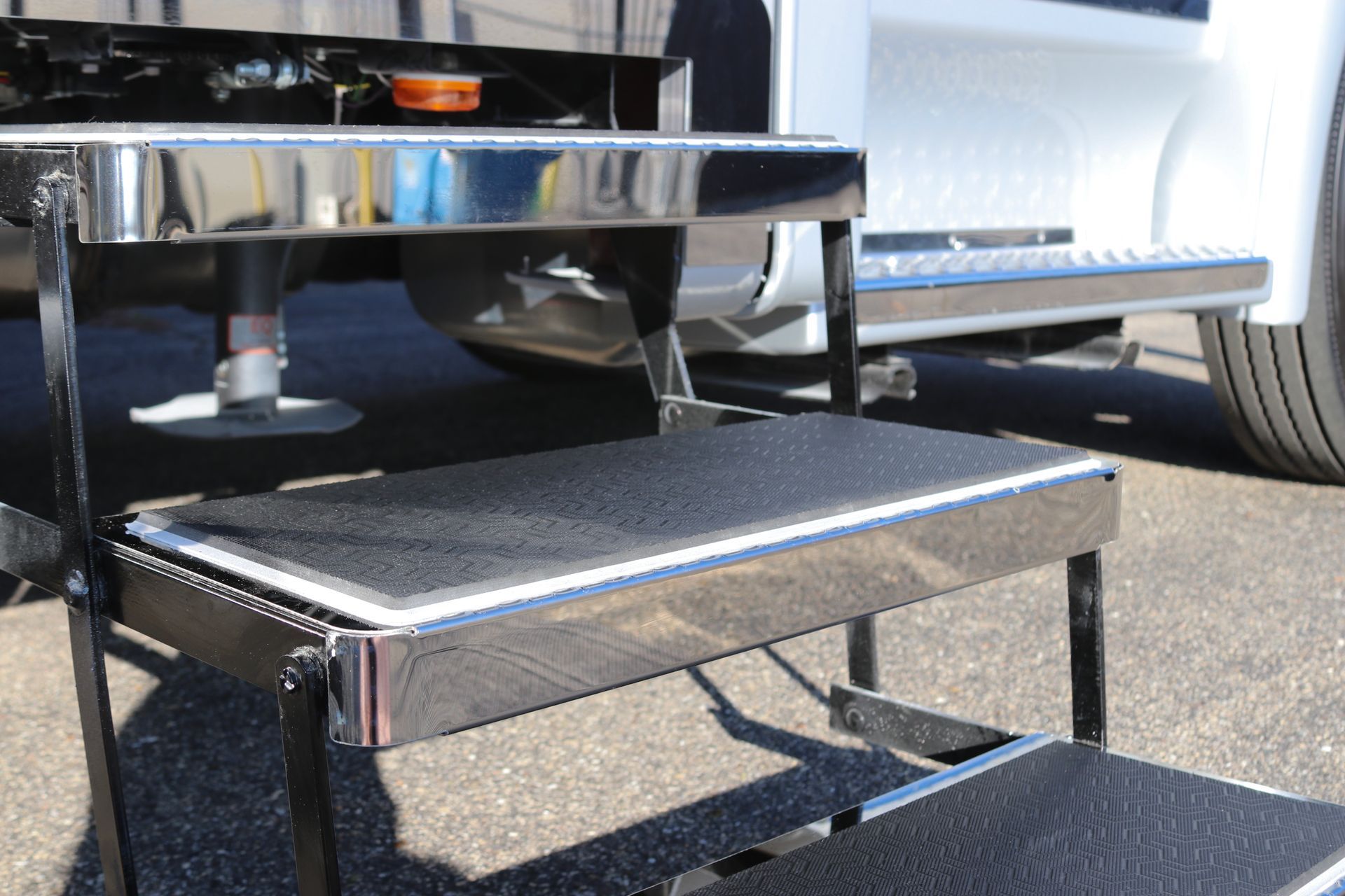 Three-step metal RV entrance with black non-slip treads, shiny chrome edging, and a portion of a white RV.